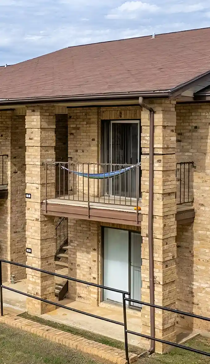 Exterior view of brick apartment building with balconies and sloped roof.