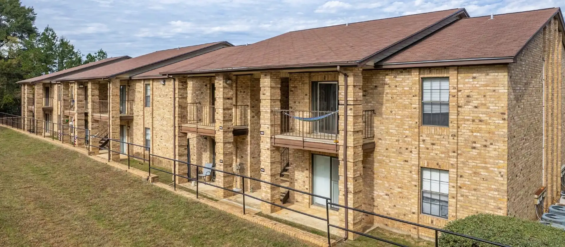 Exterior view of brick apartment building with balconies and sloped roof.